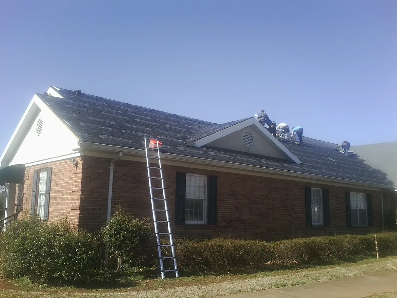Crew tearing shingles off a brick ranch roof with a ladder set — Emergency Roof Repair work by our crew in Stony Point