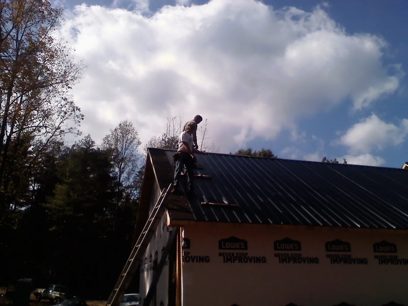 Roofer fastening dark metal panels high against a cloudy sky, from a Roof Inspection job in Stony Point