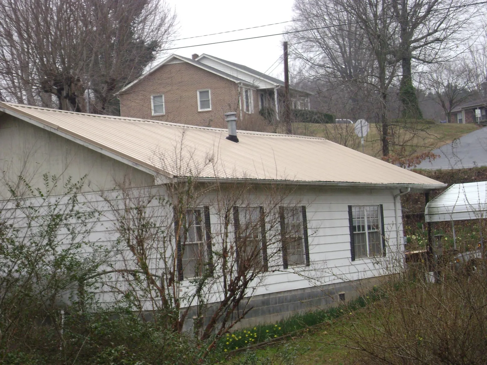 Tan metal roof on a white sided house set into a hillside — Commercial Roofing by Roofing Brothers in Stony Point